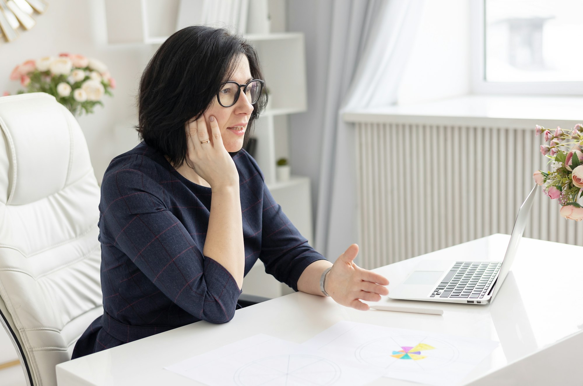 a young woman in glasses and in a blue dress works at home at a laptop as a coach