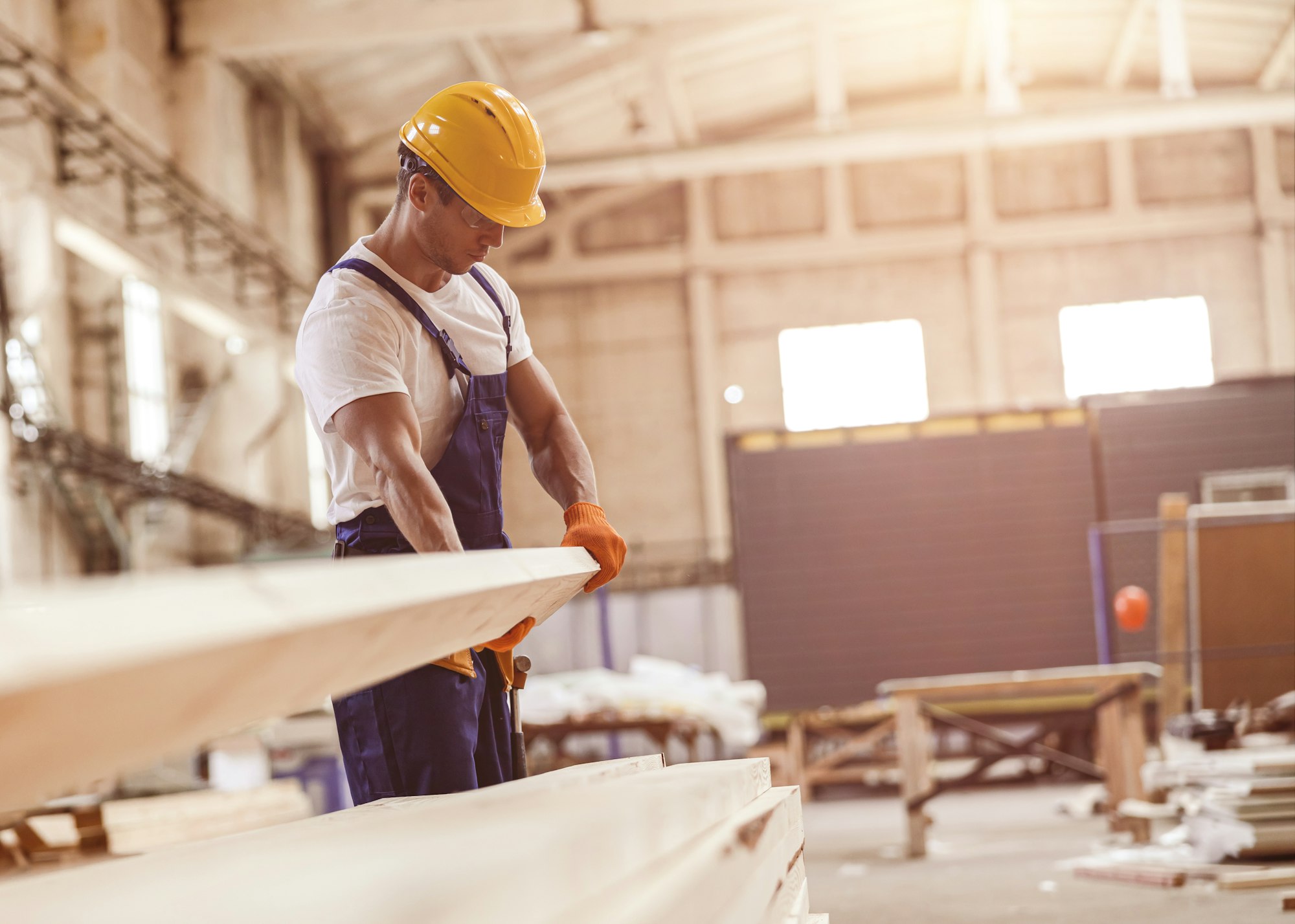 Male builder carrying wooden plank at construction site