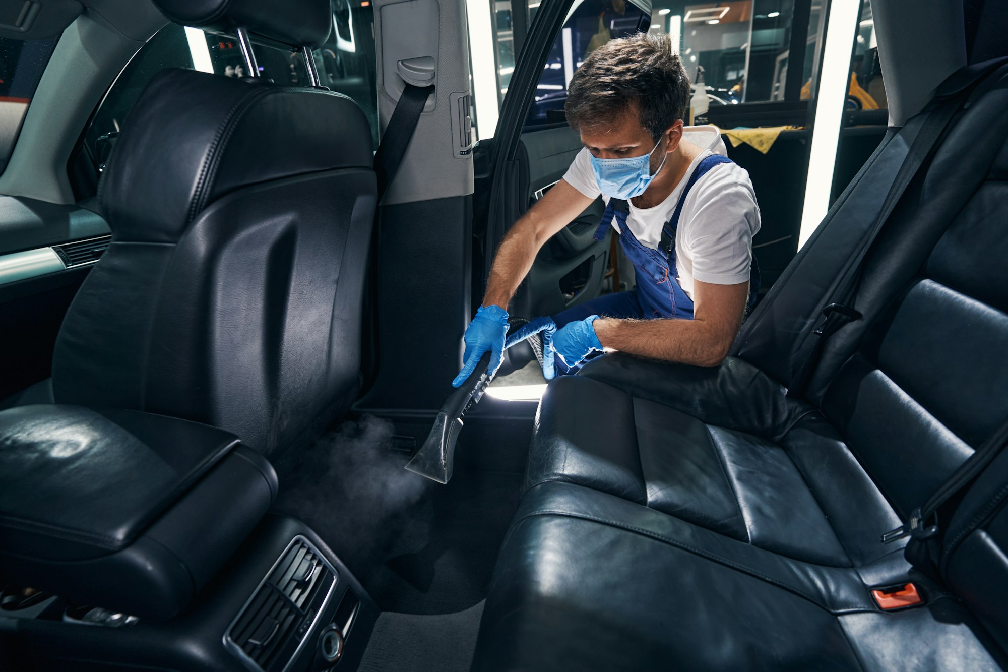 Male steam cleaning under back seats of automobile