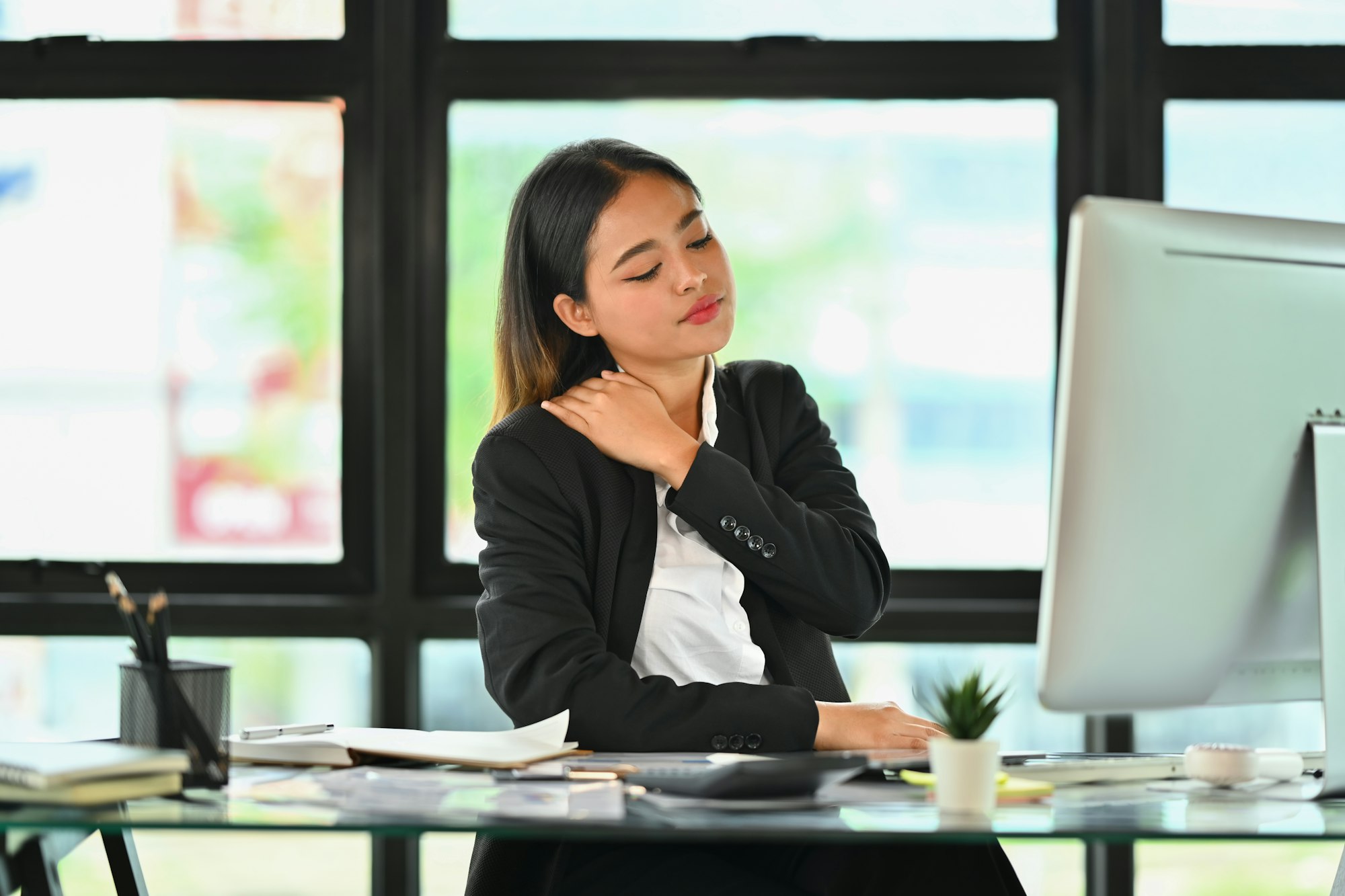 Tired millennial businesswoman massaging her neck, feeling hurt pain from incorrect posture.